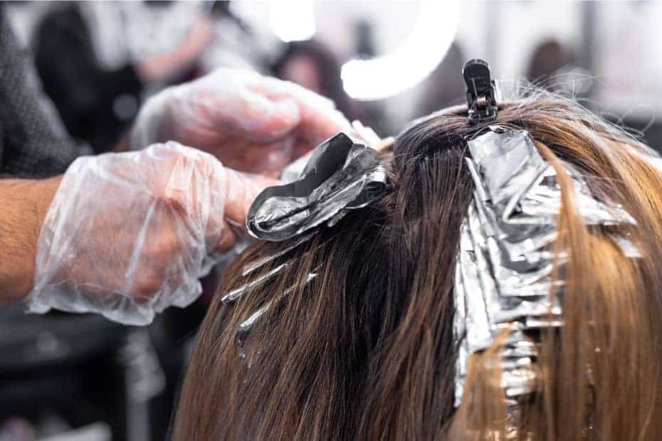 hair dresser with plastic gloves brushing on hair dye to foils in hair salon