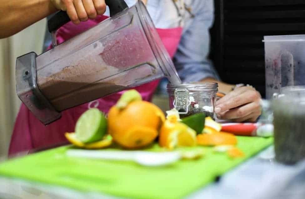 woman making her own smoothie in the kitchen with citrus fruits and vegetables
