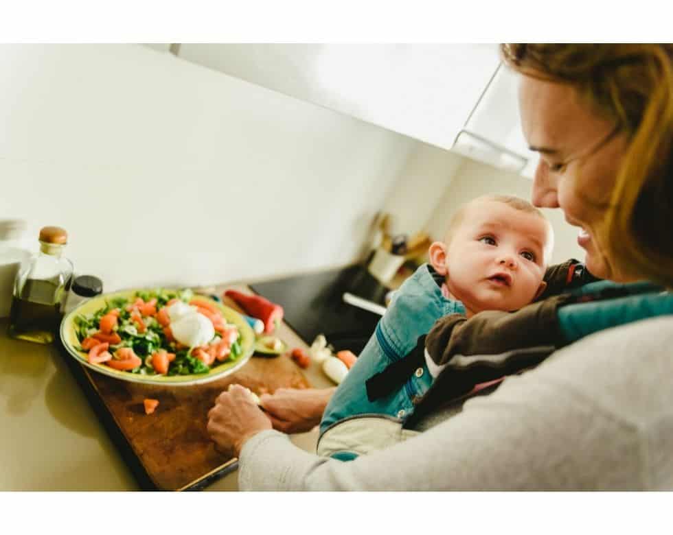 woman making a salad with a baby in a baby carrier