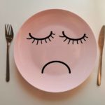 Pink dinner plate with sad face drawn on it, knife and fork on either side