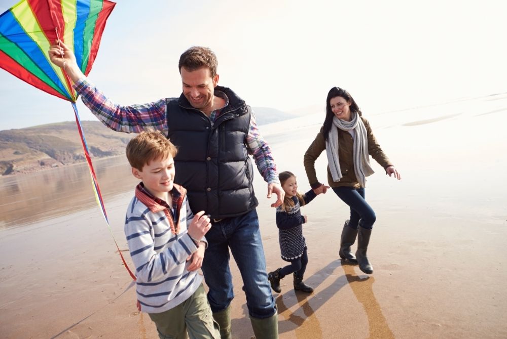 family of four at the beach flying a kite in winter