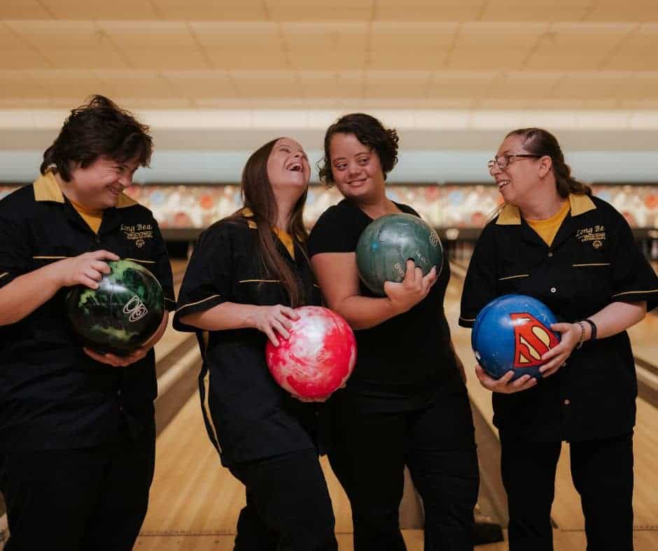 Four women, mixed ages, some with down syndrome laughing and bowling