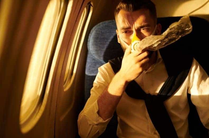 Man on an airplane with an oxygen mask over his nose and mouth looking scared